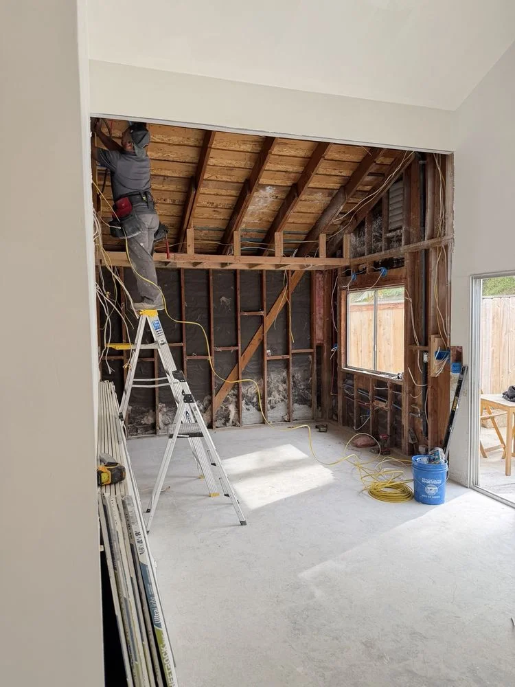 Licensed electrician performing electrical repair work on a ladder in a Vista California home, routing wiring through exposed wall framing during a residential electrical service call.