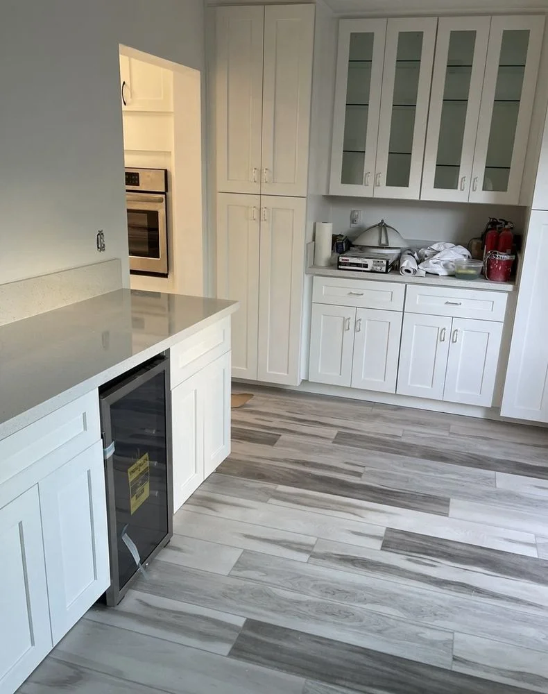 Newly installed flooring in an open-plan living area of an Encinitas, California single-family home. The finished floor runs continuously from the main living space toward a sliding glass door that opens to an outdoor patio.