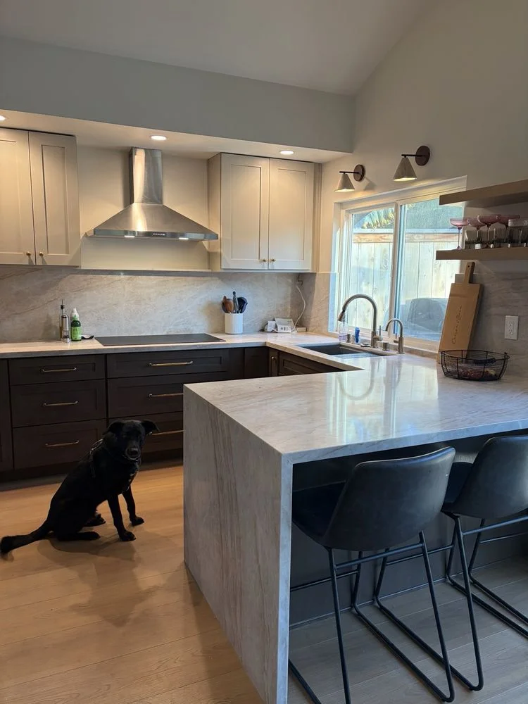A contractor and Encinitas homeowner reviewing remodeling plans inside a coastal bungalow with natural light coming through the windows. The consultation shows a floor plan layout spread across a kitchen counter with notes on proposed changes.